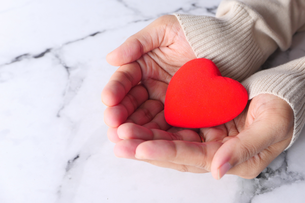 mãos de mulher recebendo coração vermelho de borracha representando óvulos doados com amor